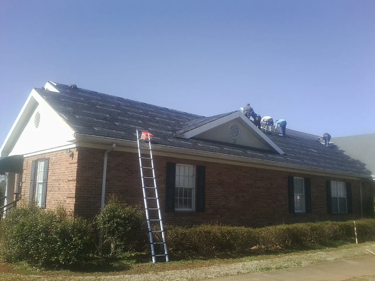 Crew tearing shingles off a brick ranch roof with a ladder set — Metal Roof Repair work by our crew in Milton Freewater