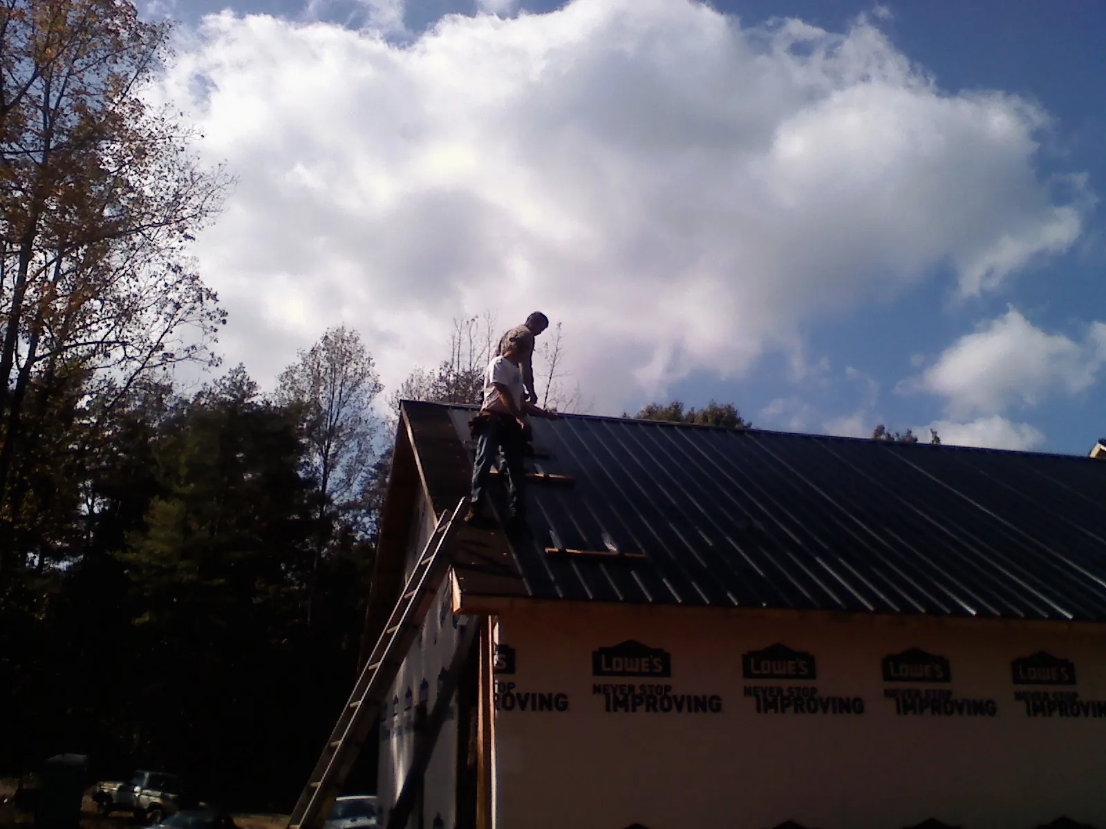 Roofer fastening dark metal panels high against a cloudy sky, from a Roof Inspection job in Milton Freewater
