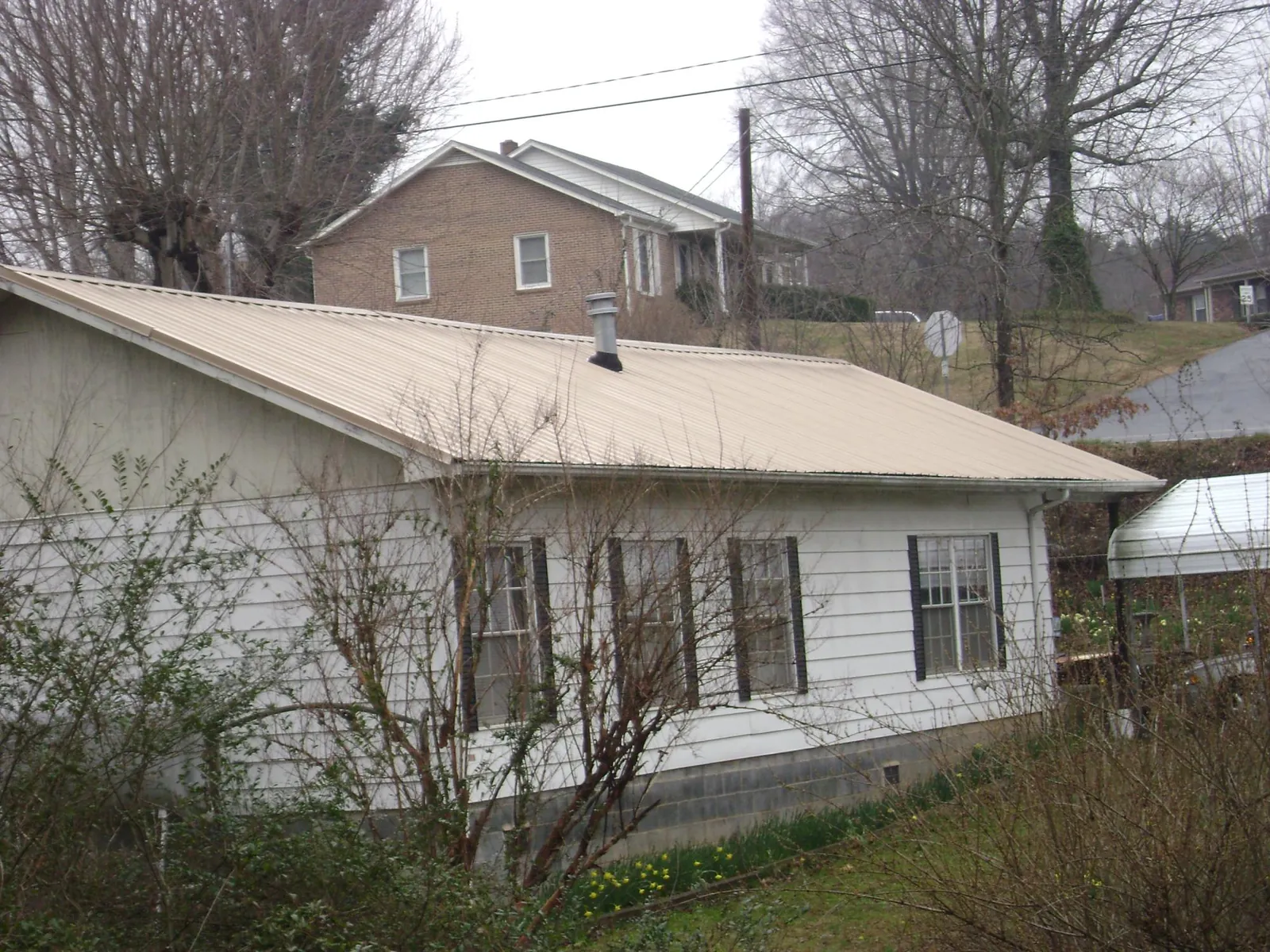 Tan metal roof on a white sided house set into a hillside — Commercial Roofing by Roofing Brothers in Milton Freewater